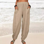 Pantalon ample en lin beige pour femme, style décontracté, poches avant, porté sur une plage ensoleillée, idéal pour l'été et les vacances.