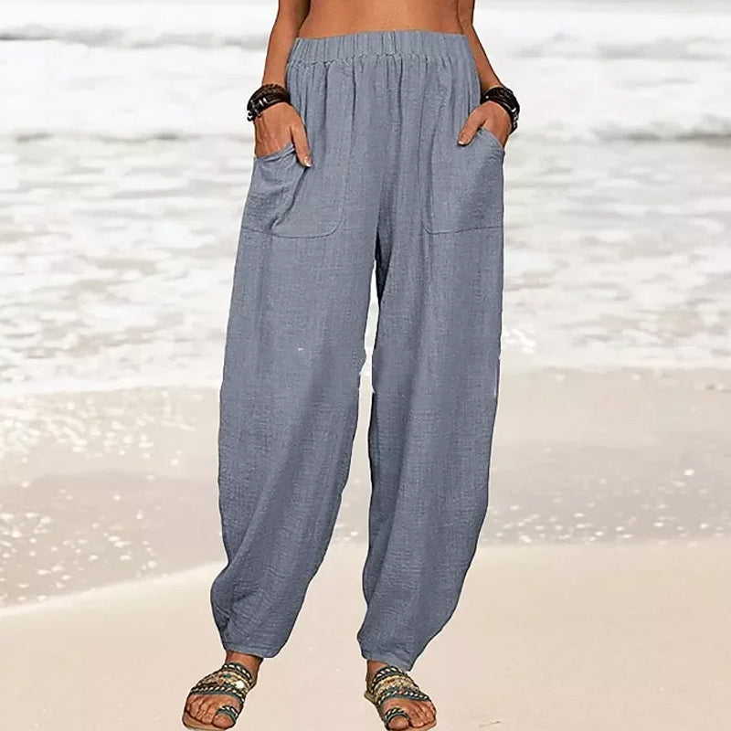 Pantalon ample en lin gris pour femme sur plage, poches avant, style décontracté, idéal pour l'été. Mode féminine, confort, vacances bord de mer.