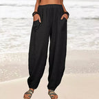 Pantalon ample noir en lin pour femme, poches avant, porté sur une plage. Mode estivale décontractée, idéal pour vacances et détente bord de mer.