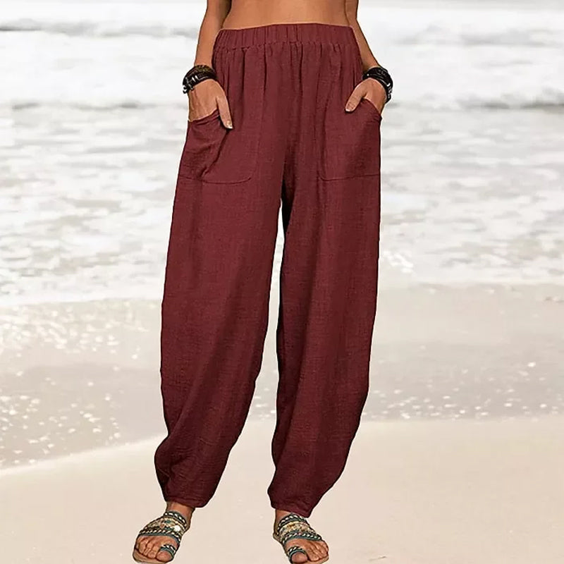 Pantalon ample en lin rouge bordeaux pour femme, poches avant, style décontracté, plage en arrière-plan, mode estivale confortable.