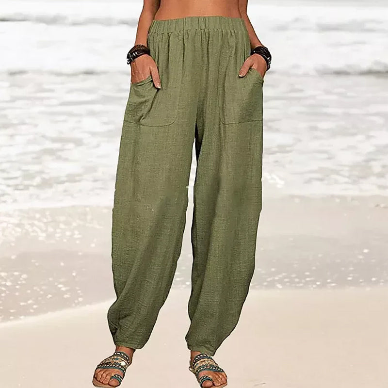 Pantalon ample en lin vert pour femme, poches avant, style décontracté, plage en arrière-plan, mode estivale, confort et élégance.
