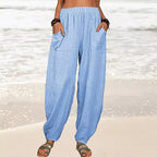 Pantalon ample en lin bleu clair pour femme, poches avant, porté sur une plage. Mode estivale décontractée, tenue de plage élégante.