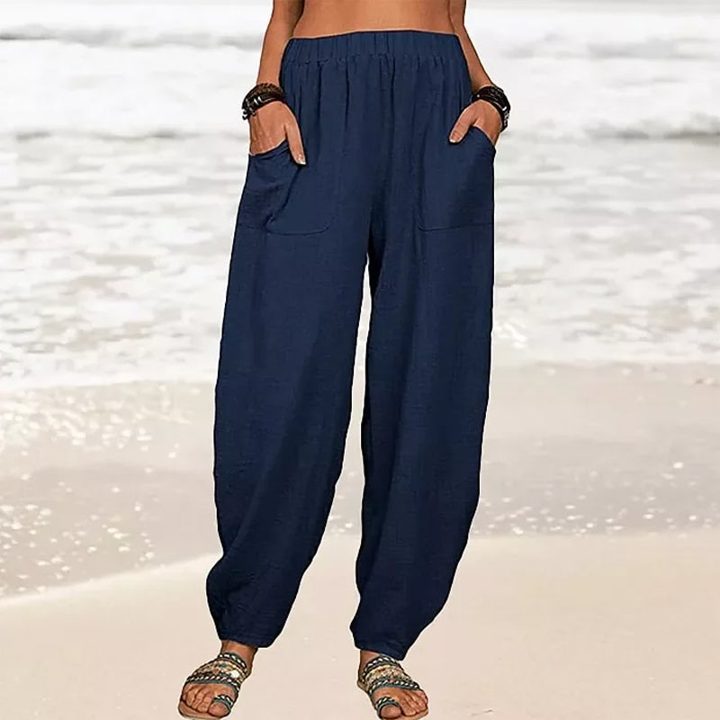 Pantalon ample bleu marine pour femme sur plage, poches latérales, style décontracté, idéal pour l'été. Mode plage, confort, tendance estivale.