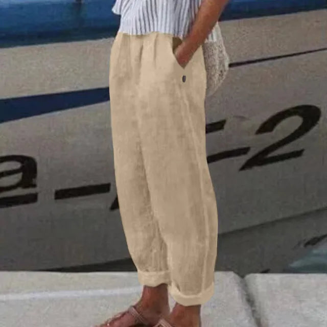 Personne portant un pantalon en lin beige et des sandales marron devant un bateau. Mode estivale décontractée, style nautique.