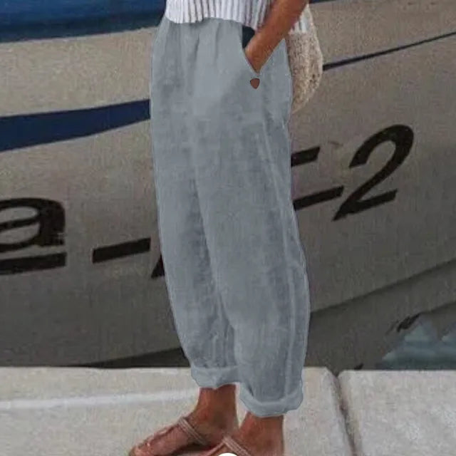 Pantalon ample gris en lin porté par une personne, debout près d'un bateau. Mode décontractée, style estival, confort et élégance.