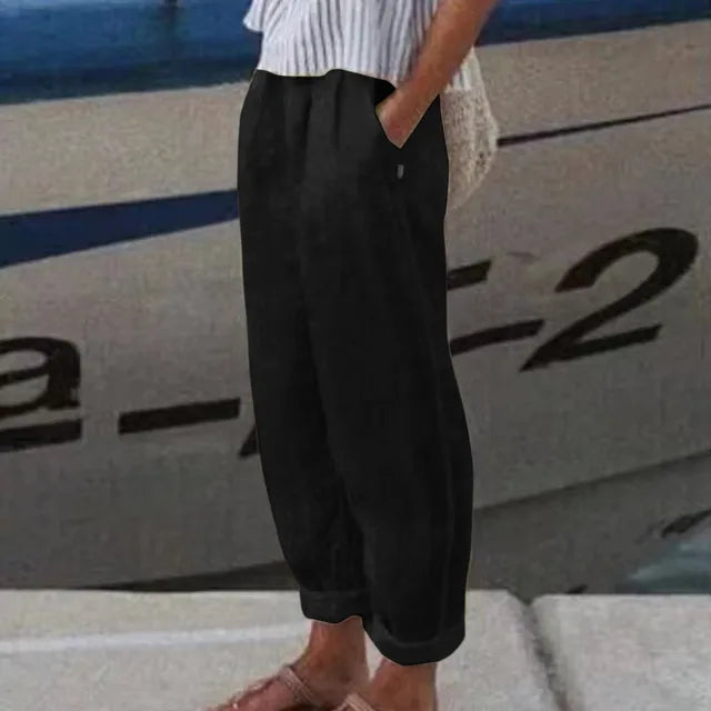 Personne portant un pantalon noir ample et des sandales, debout près d'un bateau. Mode décontractée estivale, style nautique.