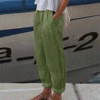 Personne portant un pantalon vert ample en lin, debout près d'un bateau. Mode décontractée, style estival, confort et élégance.