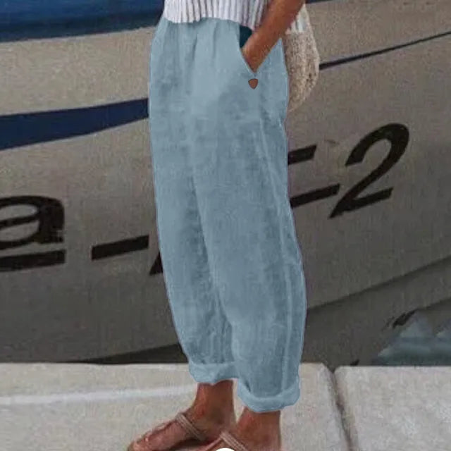 Pantalon ample en lin bleu clair, style décontracté, porté avec des sandales marron, devant un bateau. Mode estivale, confort et élégance.