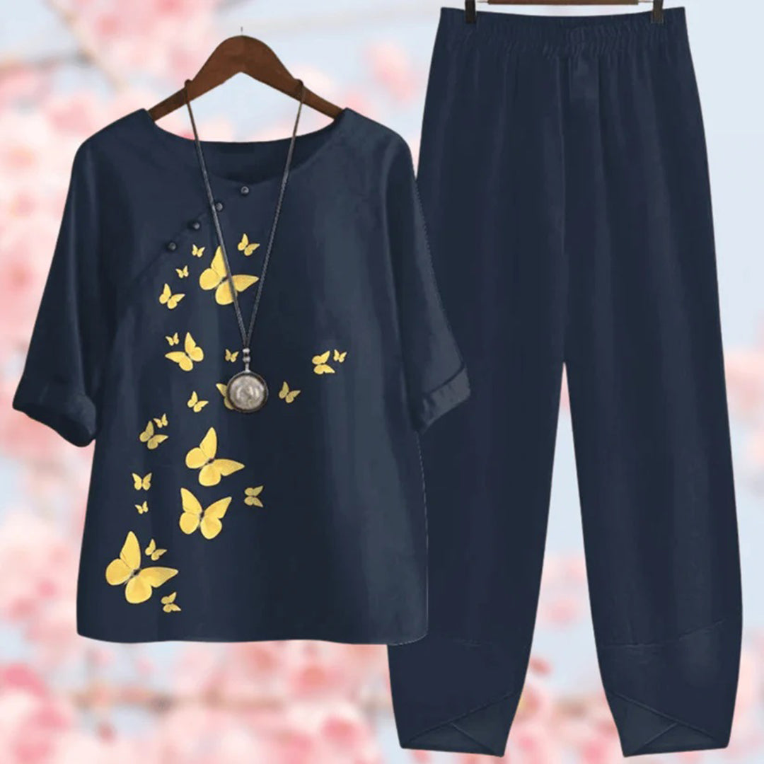 Tenue femme élégante, ensemble bleu marine avec papillons jaunes, collier pendentif, fond flou floral. Mode printemps, style décontracté chic.