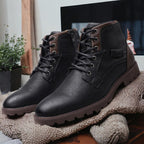 Chaussures en cuir noir pour homme, style bottines, avec lacets et semelle crantée, posées sur un tapis beige, décor moderne en arrière-plan.
