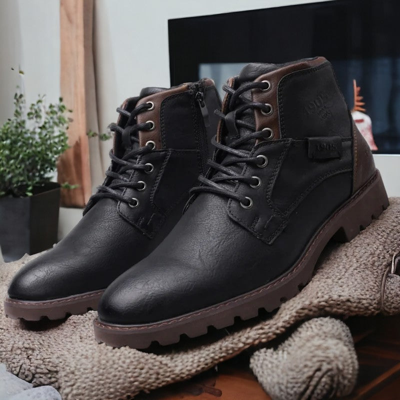 Chaussures en cuir noir pour homme, style bottines, avec lacets et semelle crantée, posées sur un tapis beige, décor moderne en arrière-plan.
