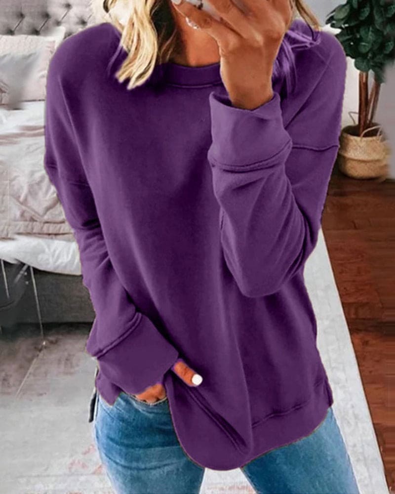 Femme portant un pull violet ample, tenant un smartphone, debout dans une chambre moderne. Mode décontractée, tendance automne-hiver.