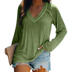 Femme portant un t-shirt vert à manches longues avec un col en V, associé à un short en jean décontracté, tenant une pochette beige.