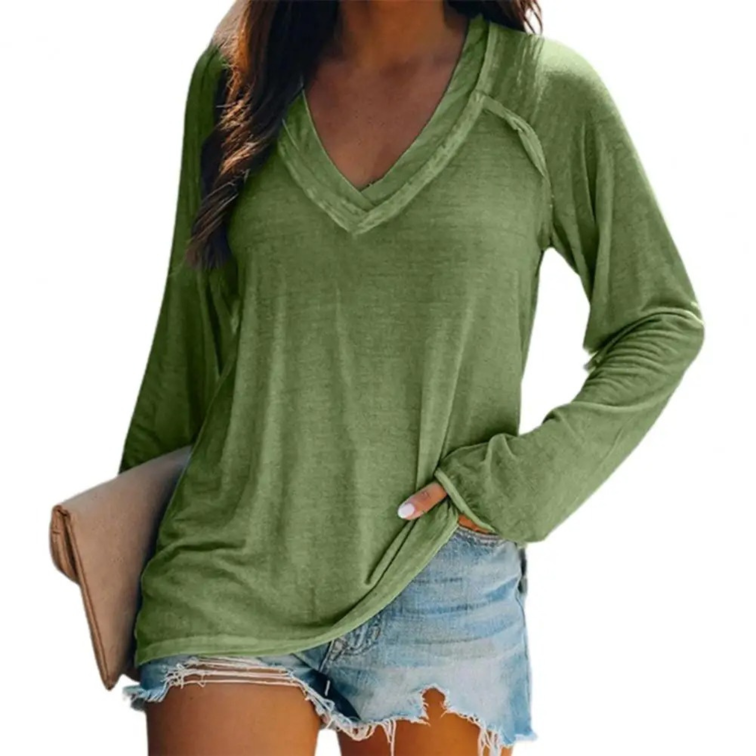 Femme portant un t-shirt vert à manches longues avec un col en V, associé à un short en jean décontracté, tenant une pochette beige.
