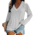 Femme portant un t-shirt blanc à manches longues avec un col en V, associée à un short en jean décontracté, tenant une pochette beige.