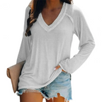 Femme portant un t-shirt blanc à manches longues avec un col en V, associée à un short en jean décontracté, tenant une pochette beige.