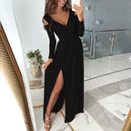 Robe longue noire élégante avec fente, manches longues, portée par une femme souriante dans un intérieur moderne. Mode féminine chic et tendance.