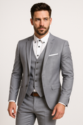 Homme en costume gris élégant, chemise blanche, cravate absente, posant sur fond neutre. Mode masculine, tenue formelle, style moderne.