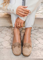 Femme portant des mocassins en daim beige avec nœuds, jeans blancs effilochés et pull crème. Mode décontractée, chaussures tendance, style élégant.