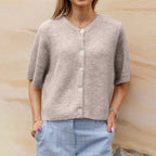 Femme portant un cardigan beige en laine avec boutons blancs, manches courtes, associé à un pantalon bleu à carreaux. Mode automne chic et décontractée.