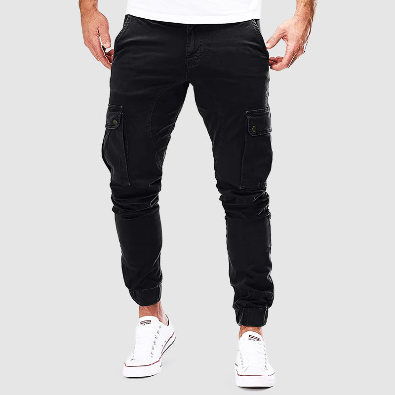 Pantalon cargo noir pour homme, style décontracté, poches latérales, coupe ajustée, idéal pour mode urbaine. Sneakers blanches visibles.