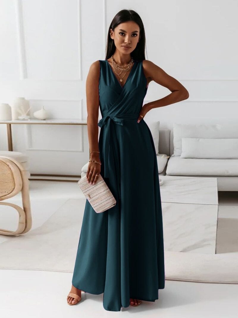 Femme portant une robe longue bleue élégante, tenant une pochette beige, posant dans un salon moderne. Mode féminine, tenue de soirée chic.