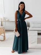 Femme portant une robe longue bleue élégante, tenant une pochette beige, posant dans un salon moderne. Mode féminine, tenue de soirée chic.