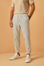 Homme portant un pantalon à rayures verticales blanches et noires, avec un t-shirt beige et des baskets blanches, sur fond beige.