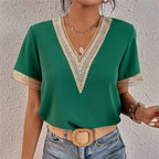 Femme portant un haut vert à col en V avec dentelle, ceinture beige, collier pendentif, et jean. Mode élégante, tenue décontractée chic.