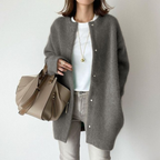 Femme portant un cardigan gris en laine, t-shirt blanc, jean clair, avec un sac à main beige. Mode automne, style décontracté chic.
