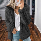 Femme portant une veste en fausse fourrure noire, t-shirt blanc et jean, tenant un smartphone, debout sur un sol en bois dans un intérieur moderne.