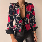 Blouse à motifs chaînes et roses rouges, manches trois-quarts, col ouvert, portée avec un pantalon en cuir noir. Mode élégante et tendance.