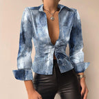 Chemisier en jean délavé bleu pour femme, manches longues, col ouvert, noué à la taille, porté avec un pantalon en cuir noir. Mode tendance.