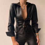 Femme portant une chemise en cuir noir élégante, ouverte, avec un collier argenté et un pantalon assorti. Mode tendance, style chic et moderne.