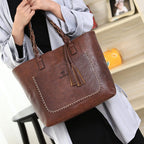 Sac à main en cuir marron avec coutures apparentes et pompons, porté par une personne en manteau gris. Accessoire mode élégant et tendance.