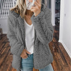 Femme portant une veste en fausse fourrure grise, t-shirt blanc et jean, tenant un smartphone. Mode automne-hiver, style décontracté.
