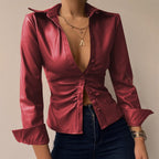 Femme portant une chemise en cuir rouge élégante, col ouvert, manches longues, avec collier doré et montre, style mode tendance.