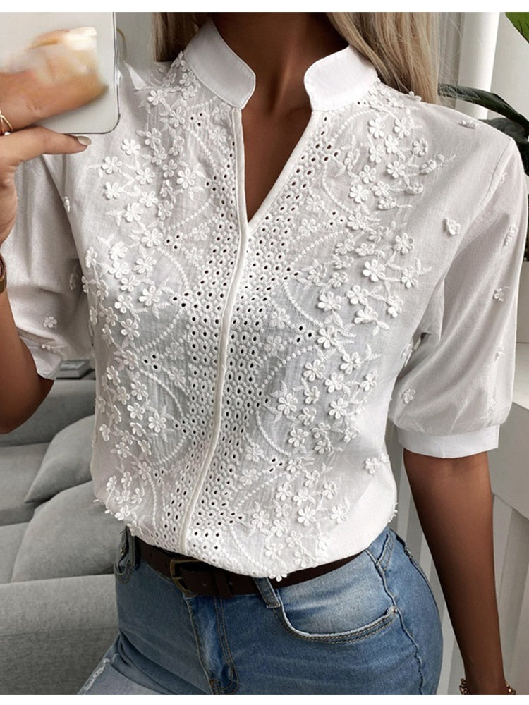 Blouse blanche en dentelle florale, manches courtes, col montant, portée avec un jean bleu. Mode féminine élégante et chic.