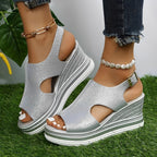 Sandales compensées argentées pour femme avec talons plateforme, portées avec un jean et bracelets de cheville, posées sur gazon vert.