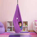 Enfant dans une balançoire hamac violet suspendue, chambre rose avec étagère blanche, jouets et coussins colorés. Confort et détente pour enfants.