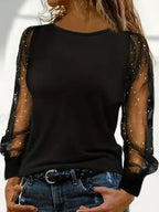 Femme portant un haut noir élégant avec manches transparentes à paillettes, associée à un jean décontracté. Mode féminine chic et moderne.