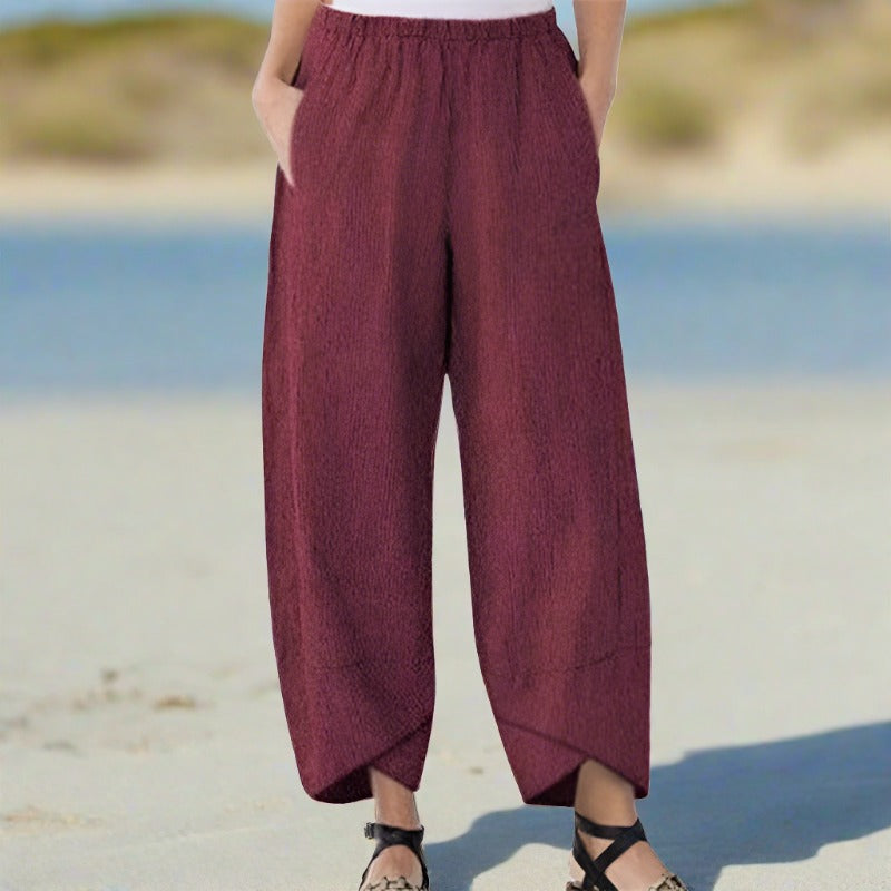 Pantalon ample bordeaux en lin pour femme, style décontracté, avec poches, porté sur une plage ensoleillée. Mode estivale confortable.