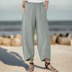 Pantalon ample en lin gris pour femme, style décontracté, avec poches, porté sur une plage en arrière-plan. Mode estivale confortable.