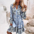 Robe fleurie bleue à manches longues, femme blonde tenant une pochette bleue, style bohème chic, intérieur lumineux, mode tendance.