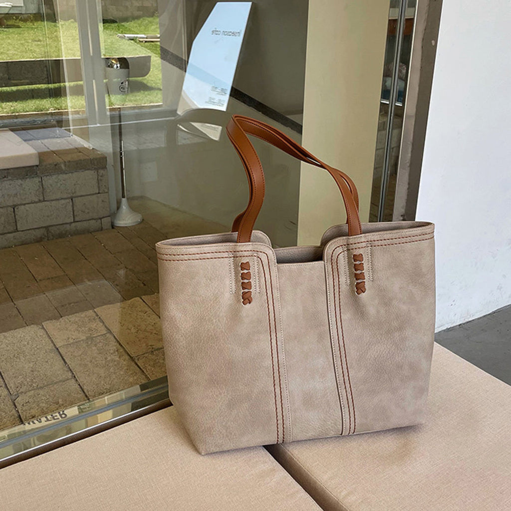 Sac à main en cuir beige avec anses marron posé sur une table, devant une vitrine. Accessoire de mode élégant pour femme, tendance et chic.