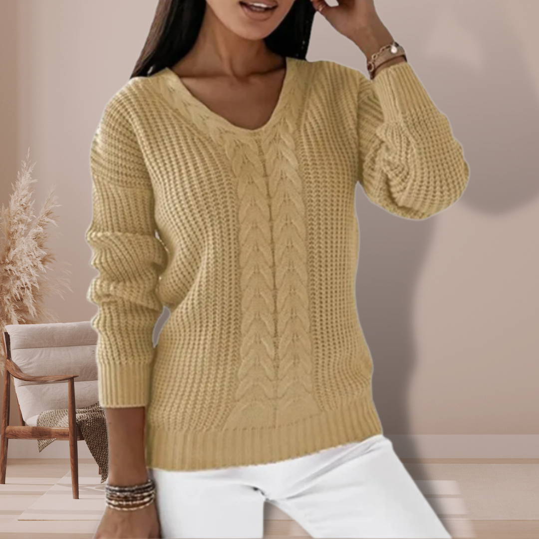 Femme portant un pull en tricot beige avec motif torsadé, manches longues, dans un intérieur moderne. Mode automne-hiver, style décontracté élégant.