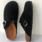 Sabots noirs en daim avec semelle en liège, boucle métallique argentée, design ergonomique, confort et style, chaussures tendance pour hommes et femmes.