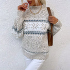 Femme portant un pull en tricot beige et blanc à motifs nordiques, col roulé, avec un sac marron, posant contre un mur blanc. Mode hiver élégante.