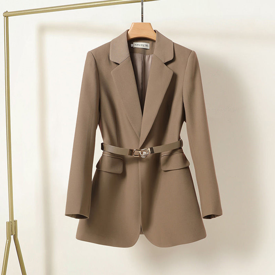 Veste blazer femme beige élégante avec ceinture, suspendue sur cintre. Mode chic, vêtement tendance pour bureau ou soirée.