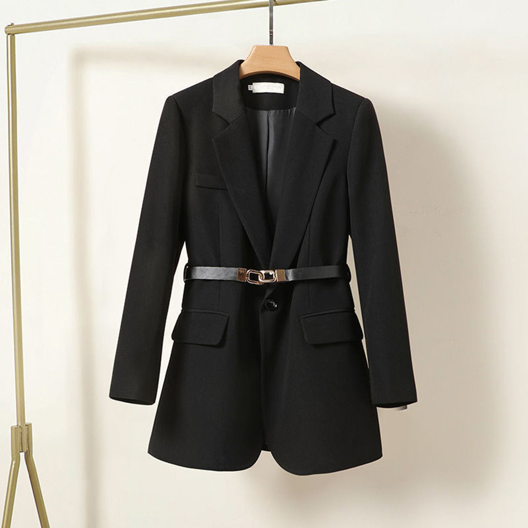 Veste blazer noire élégante avec ceinture, suspendue sur un cintre doré. Mode femme, tenue professionnelle chic, tendance automne-hiver.